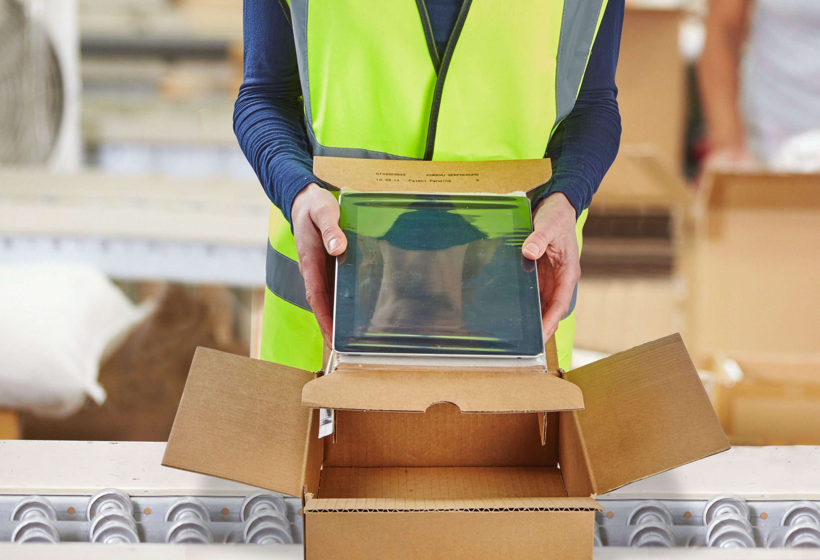 warehouse operator in neon green vest placing a tablet into a cardboard box